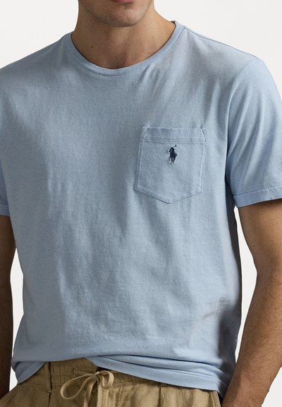 Light blue cotton T-shirt with a round neck, short sleeves, and a chest pocket featuring a small embroidered logo. Smooth texture.