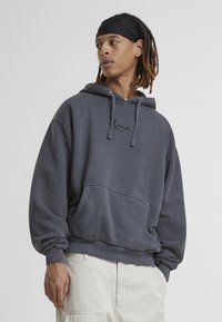 Felpa grigia in cotone con tasca frontale, cappuccio con stringhe e logo ricamato. Presenta una vestibilità comoda e polsini e bordo a costine.