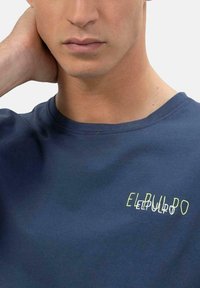 Camiseta de algodón de color azul marino con el texto "EL PULPO" en una mezcla de amarillo brillante y blanco, cuello redondo y mangas cortas. Textura suave.