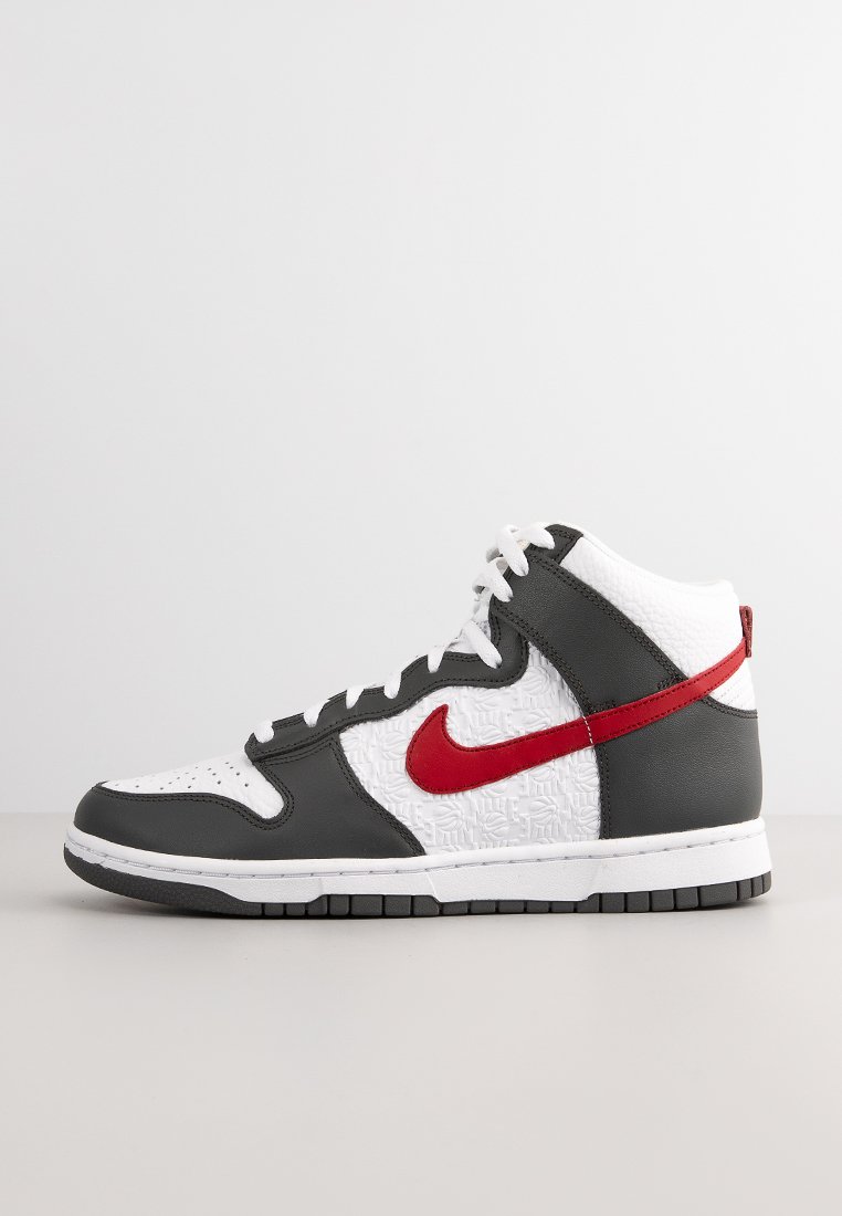 Baskets montantes avec une boîte à orteils en cuir blanc, des panneaux texturés blancs, un corps en cuir gris, et un swoosh et des accents rouges de Nike. Semelle en caoutchouc noir.