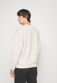 Lichtbeige sweatshirt met een gestructureerd patroon, quilted ontwerp en geribbelde manchetten. Heeft een ronde hals en een ontspannen pasvorm.