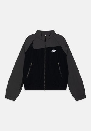 Sort og mørkegrå Nike jakke med fuld lynlås foran, lynlåslommer i siderne, elastiske manchetter og hvid Nike-logo på brystet.