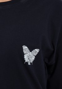 Navyblaue Baumwoll-T-Shirt mit langen Ärmeln, das ein weißes Schmetterlingsgrafik mit feinen Linien und markentext unter dem Design zeigt.