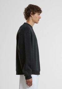 Schwarzer Rundhalsausschnitt-Hoodie mit langen Ärmeln, gerippten Bündchen und einem lockeren Schnitt, aus weichem Material, seitlich präsentiert.