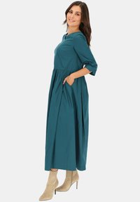 Turkusowa sukienka z długim rękawem, z marszczoną talią, kieszeniami po bokach i okrągłym dekoltem, w zestawie z beżowymi, spiczastymi botkami za kostkę.
