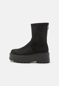 Bota de ante negro hasta la mitad de la pantorrilla con suela gruesa de plataforma, suela exterior acanalada, cremallera en la parte trasera y sutil logo "cK" cerca de la parte superior.