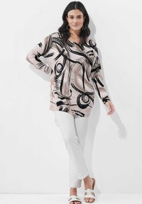 Übergroßer, langärmeliger Oberteil in Pink mit schwarzen abstrakten Mustern. Kombiniert mit weißen Slim-Pants und weißen Sandalen. Glattes Material, lässiger Schnitt.