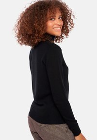 Schwarzer Rollkragenpullover aus weichem Strick, figurbetontes Design, lange Ärmel, mit glatter Textur und geripptem Saum, kombiniert mit strukturierten braunen Hosen.