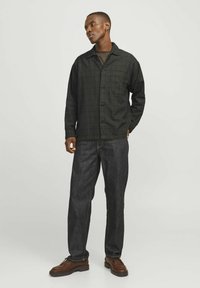Cămașă cu carouri negre, cu un singur buzunar pe piept, asortată cu pantaloni din denim închis la culoare și pantofi maro. Cămașa are un design cu nasturi.