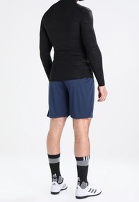 Czarna sportowa bluzka z długim rękawem, niebieskie szorty, czarno-białe skarpetki w paski oraz białe trampki z czarnymi akcentami.