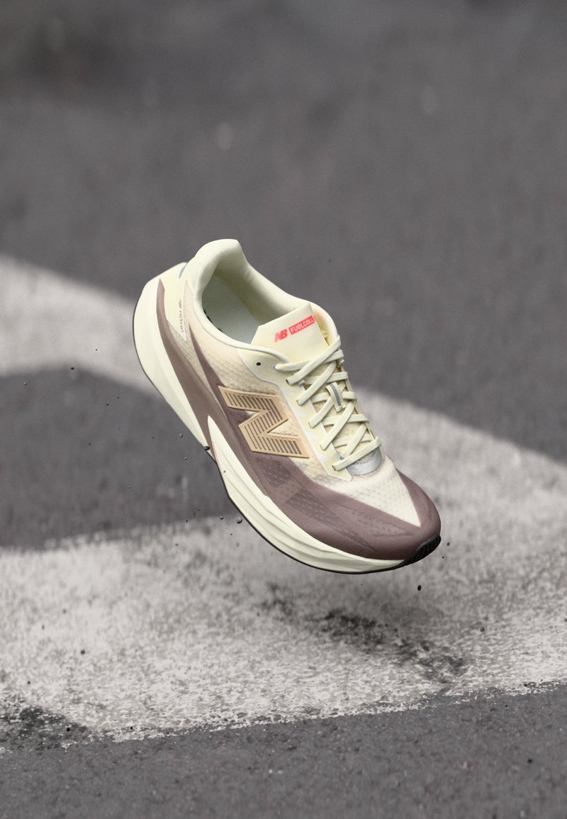 Lightweight athletic shoe with a cream upper and brown accents, featuring a textured surface, laces, and a prominent logo on the side.