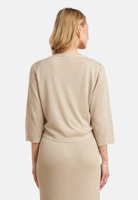 Beige sparkly knit top with three-quarter sleeves, round neckline, and a relaxed fit, paired with a matching ribbed skirt.