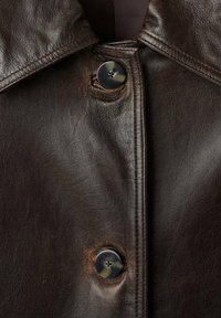 Chaqueta de cuero marrón con un gran cuello, que presenta un cierre de botón prominente. Textura suave con ligeras arrugas y detalles de desgaste.