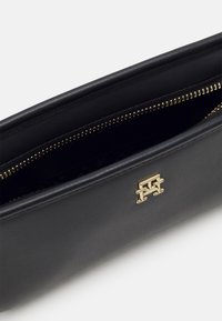 Clutch in pelle nera con hardware dorato, chiusura con zip e texture liscia. Presenta un accento con logo sulla parte anteriore. L'interno è decorato con un motivo.