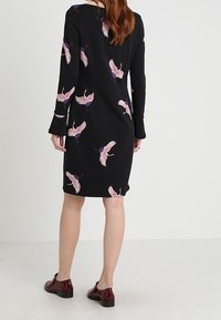 Robe noire à manches longues ornée d'un motif de grues rose et bleu. Modèle mi-long avec une texture lisse et un décolleté simple.