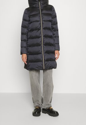 Sort quiltet lang puffjakke med lynlås foran, båret med grå jeans med vidde og sorte loafers med gulddetalje.