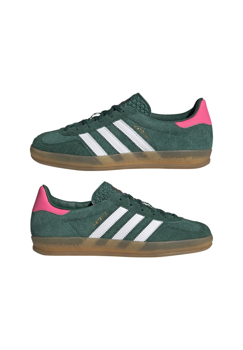 Sneaker in suede verde con strisce bianche e dettagli rosa. Suola in gomma trasparente. La parte frontale mostra i lacci; i lati presentano dettagli testurizzati vicino al tallone.