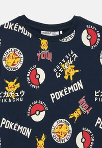 Sötétkék pulóver Pikachu illusztrációkkal, Pokéballokkal, és szövegekkel, mint például "TÉGED VÁLASZTLAK!" különböző betűtípusokban és elrendezésekben. Pamut anyag.