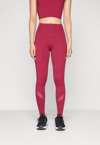 High-waisted maroon leggings with a smooth texture, mesh panels at the calves, and a fitted design, paired with black athletic shoes.