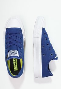 Niebieskie płócienne trampki z białymi gumowymi podeszwami i oczkami. Posiadają okrągły nosek, sznurowany fason oraz kontrastowe zielone wykończenie wewnętrzne.