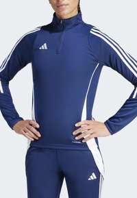 Jūras spēku sporta tops ar augstu apkakli, baltām sānu akcentiem un trim baltām svītrām uz piedurknēm. Izgatavots no elpojoša materiāla, ar zīmolu "AEROREADY."