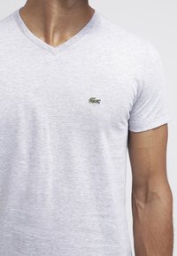 Gray cotton v-neck t-shirt with short sleeves, featuring a small green embroidered crocodile logo on the left chest area.