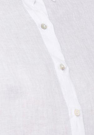 Tessuto di lino bianco con una fila verticale di tre bottoni beige chiaro lungo una patta.
