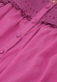 Lichtroze jurk met een textuur en geborduurde inzet. Bevat stoffen knopen en een gegolfde rand, wat extra detail aan het ontwerp toevoegt.