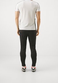 Fazovaný bílý sportovní triko s černými akcenty, spárované s černými sportovními kalhotami a kopačkami s červenými detaily na patách.