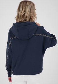 Sudadera con capucha de color azul marino, con puños acanalados, de corte holgado y con una impresión de marca a lo largo de los hombros. Tejido suave con un acabado texturizado.
