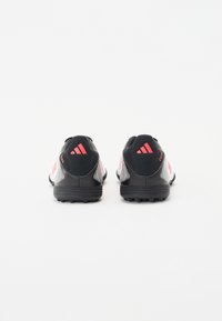 Schwarz-weiße Sportschuhe mit roten Akzenten, die über ein elegantes Design, eine strukturierte Oberseite und Gummisohlen mit spitzenähnlichen Profilen verfügen.