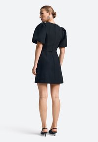 Schwarzes kurzes Kleid mit strukturierten Puffärmeln, tailliertem Schnitt und glatter Textur. Verfügt über einen versteckten Reißverschluss im Rücken und einen Saum, der oberhalb des Knies endet.