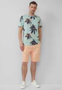 Korte mouw lichtblauwe T-shirt met palmbomenprint in marineblauw en koraal, gecombineerd met perzik kleurige shorts en witte sneakers. Schoon ontwerp, casual uitstraling.