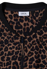 Tissu marron et noir imprimé léopard avec col noir et fermeture éclair noire centrale, montrant une étiquette blanche indiquant le nom de la marque Cecil.