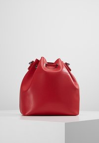 Rød læderspandtaske med rund bund, snøret top og sølvhardware. Glat tekstur med et minimalistisk design.