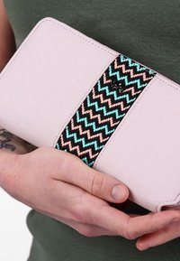 Pink fabric clutch with zigzag patterned woven accent. Clutch features a smooth texture, rounded corners, and neutral-toned design.