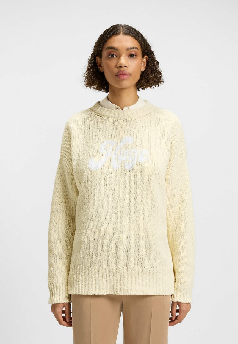 Maglione giallo lavorato a maglia con orlo a coste. Presenta un logo bianco "Hugo" sulla parte anteriore e un design con spalla cadente. Tessuto testurizzato con vestibilità ampia.