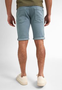 Pantalones cortos de mezclilla azul claro con dobladillos enrollados, que cuentan con dos bolsillos traseros y detalles de costura sutiles. Llevados con zapatillas blancas.