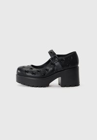Black platform shoes with a rounded toe, featuring circular cutouts, a buckle strap, and a textured rubber sole for traction.