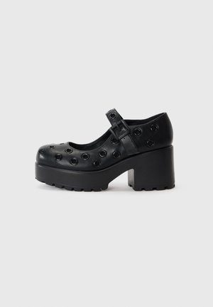 Black platform shoes with a rounded toe, featuring circular cutouts, a buckle strap, and a textured rubber sole for traction.