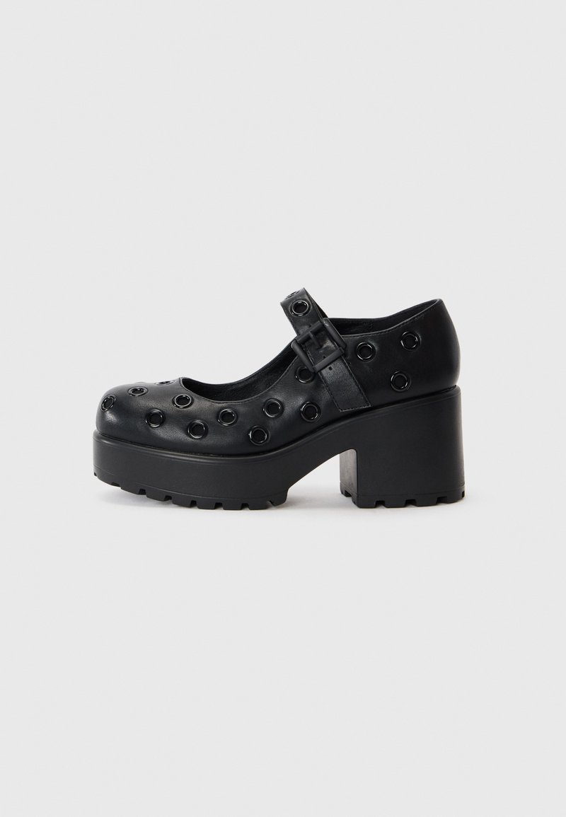 Black platform shoes with a rounded toe, featuring circular cutouts, a buckle strap, and a textured rubber sole for traction.