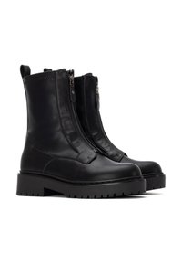 Botas de cuero negras hasta el tobillo con dos cremalleras laterales, suela de goma negra gruesa y detalles de costura mínimos en la parte superior.