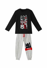Schwarzes Langarmshirt mit dem Text "MONSTER MACHEN MIR KEINE ANGST!", kombiniert mit grauen Hosen, die eine Monstergrafik und rote Akzente aufweisen.