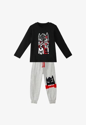 Czarna koszula z długim rękawem z napisem "MONSTERS DON'T SCARE ME!" w połączeniu z szarymi spodniami z grafiką potwora i czerwonymi akcentami.