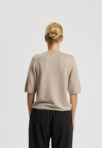 Maglione beige in maglia con maniche corte e colletto a girocollo. La texture è liscia, con un fit rilassato e sottili dettagli a coste all'orlo.