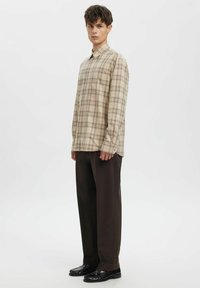 Beežikas ruuduline pika varrukaga särk, mida kannavad tumepruunide pükstega ja mustade nahkkontsakingadega. Särgil on klassikaline krae.