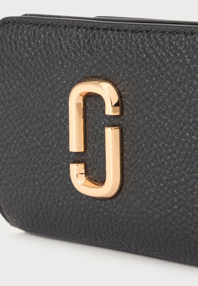 Surface en cuir noir texturé avec un logo métallique doré brillant en forme de double J attaché.