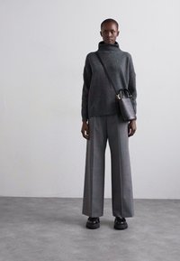 Pull en maille gris foncé surdimensionné avec un col haut, associé à un pantalon large gris clair bien ajusté. Petit sac à main noir avec une bandoulière.