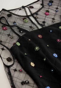 Schwarzes Kleid mit einem durchsichtigen Netzüberzug, das mit bunten, gestickten Blumenmustern verziert ist. Die innere Schicht ist einfarbig schwarz und verfügt über verstellbare Träger.