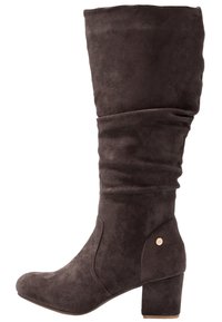 Bota de ante marrón hasta la rodilla con un diseño ligeramente caído, puntera redondeada y un tacón grueso. Presenta un acento dorado cerca del tacón.